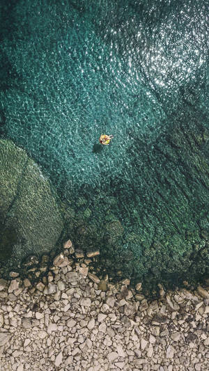 一個人漂浮在黃色充氣圈上，在岩石海岸附近清澈的碧綠海水中。
