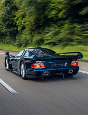 深藍色 Mercedes CLK GTR 在穿越綠色森林的道路上疾馳。 — 藍色 壁紙