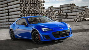 藍色Subaru BRZ跑車停在工業管道堆附近。