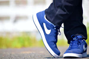 藍色Nike運動鞋帶白色swoosh標誌，配深色牛仔褲，在碎石路上。 — 卡通鞋 壁紙
