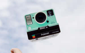 一部薄荷綠色的Polaroid相機漂浮在空中，由一根手指從下方托住。
