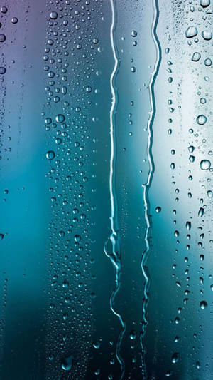 雨滴在帶有青綠色和藍色調的玻璃表面上滑落的特寫。