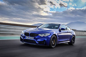 藍色BMW M4 Coupe在賽道上飛馳，背景有山脈和多雲天空。 — 藍色 壁紙