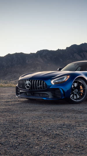 日落時分，藍色 Mercedes-AMG GT 跑車停泊在山附近的碎石上。