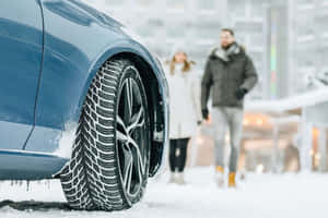 一輛藍色汽車，輪胎上有雪，一對情侶在雪中行走。 — 低調 壁紙