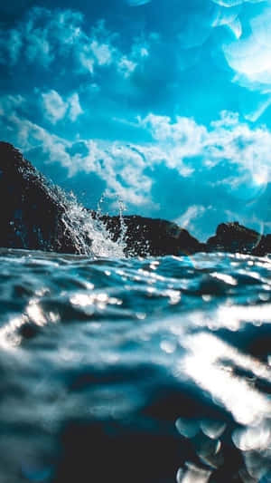 海浪拍打深色岩石，上方是明亮的藍天和白雲。
