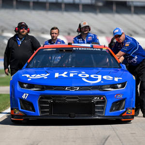 帶有Kroger標誌的藍色NASCAR賽車在賽道上被團隊工作人員推動。