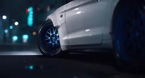 霓虹燈下，夜晚潮濕的城市街道上的白色汽車，藍色車輪。