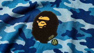 藍色迷彩連帽衛衣，帶有棕色Bape猿頭補丁和綠色標誌。 — Bape GIF 壁紙