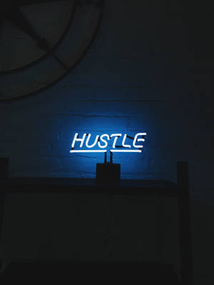 藍色霓虹燈牌，在暗色磚牆上顯示 HUSTLE。