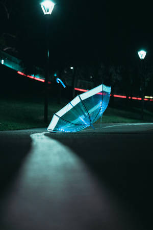 一把發光的藍色雨傘在夜晚街燈下躺在濕漉漉的人行道上。