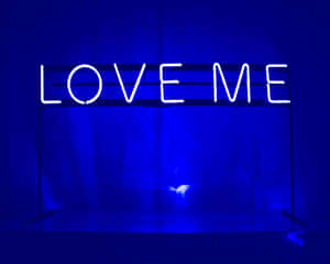 一個發光的霓虹燈牌，上面寫著 LOVE ME，在昏暗的藍色燈光房間中。