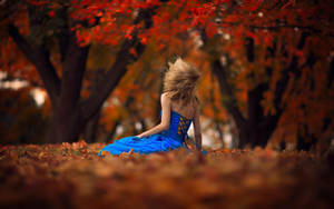 藍裙女性坐在秋葉上，紅樹下