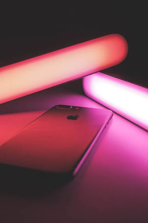 iPhone在黑暗的表面上被粉紅色和紅色的霓虹燈照亮。
