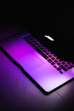 在黑暗中，木桌上發光的紫色筆記型電腦。