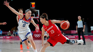 日本籃球運動員在奧運比賽中運球越過美國防守球員。