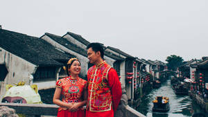 一對幸福的新人穿著傳統紅色婚禮服飾，在歷史悠久的中國水鄉的運河橋上。 — 唐人街 GIF 壁紙