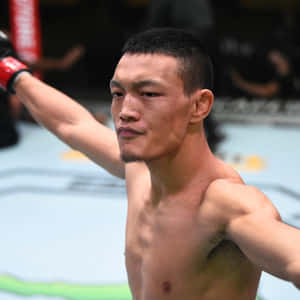 一位赤裸上身的MMA拳手在八角籠內舉起戴著紅色手套的拳頭慶祝勝利。