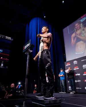 UFC拳手在稱重活動中站在體重磅上，屏幕顯示對手