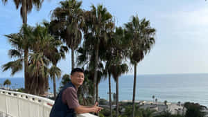 男子在陽台上微笑，身後是海洋和棕櫚樹