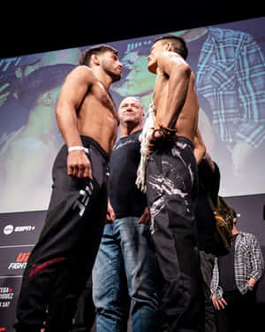 兩位赤裸上身的MMA拳手在稱重活動中對視，中間有一位裁判。