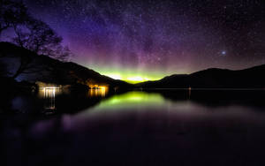 北極光在夜晚的星空湖上閃耀，山巒剪影。
