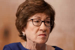 一位戴眼鏡、身穿藍色上衣的嚴肅年長女性的特寫。 — 政治 壁紙
