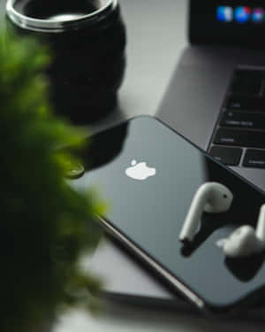 黑色iPhone配白色耳機，與手提電腦和相機鏡頭一起放在有綠色植物的桌子上。