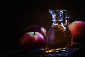 玻璃壺蘋果酒與紅蘋果在木質表面上，光線昏暗