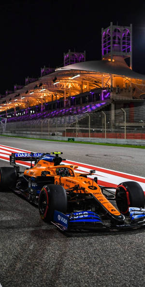 夜間賽道上橙色和藍色的F1賽車，看台燈光璀璨。
