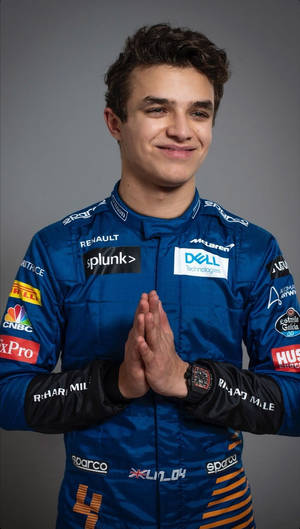 年輕男性賽車手身穿藍色McLaren賽車服，雙手合十微笑。