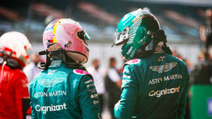 兩位身穿青綠色Aston Martin賽車服的F1車手在賽道上交談。