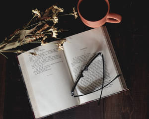 打開的書、眼鏡和杯子在木桌上，配有乾花