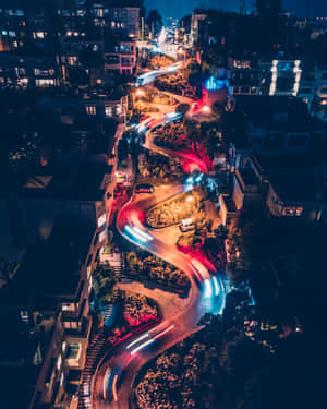 夜間蜿蜒的城市街道，帶有汽車燈光條紋和明亮的房屋。 — 明亮 壁紙