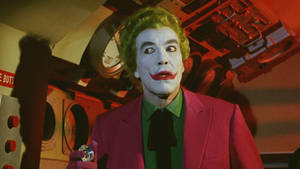 小丑穿著粉紅色西裝，綠色頭髮和紅色嘴唇，在控制室裡。 — 小丑 壁紙
