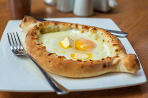 Khachapuri 麵包碗配雞蛋和牛油，放在白色碟上，附有叉子。