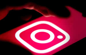 手在夜間懸浮在發光的Instagram應用程式圖標上方。