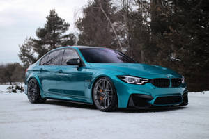 綠松石色BMW M3房車停泊喺樹附近嘅雪地上。