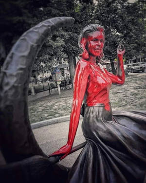 一座漆成紅色的女性雕像，穿著黑色裙子，在公園中透過彎曲的拱門觀看。