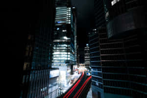 夜晚高聳的城市建築，帶有移動汽車的紅色光條。
