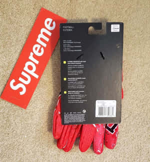 紅色 Supreme 美式足球手套原裝包裝放在米色地毯上。