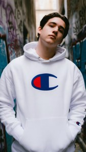 年輕男子身穿白色Champion連帽衫站在塗鴉小巷