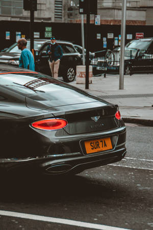 黑色賓利 Continental GT 帶紅色尾燈停泊在濕漉漉的城市街道上。