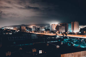 夜晚城市景色，有發光的建築物和一座橋樑，天空多雲。