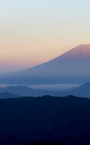 黎明時分的富士山，層疊山巒輪廓上空有粉紅色和藍色的天空。 — Galaxy Tab S9 FE 壁紙