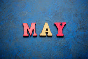 在藍色紋理表面上拼出「MAY」的木製字母。