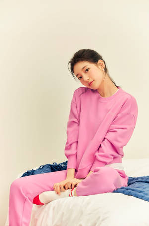 年輕女性穿著粉紅色家居服，平靜地坐在床上。