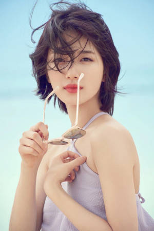 女性在微風吹拂的海灘日將太陽眼鏡貼在唇邊。