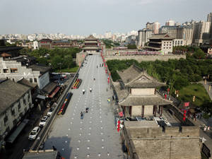 古代中國城牆，遊客沿著鋪砌的小路行走，周圍是傳統和現代建築。 — 中國 壁紙