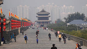 人們在歷史悠久的石牆上騎單車和散步，背景有紅色燈籠和現代建築。 — 唐人街 GIF 壁紙
